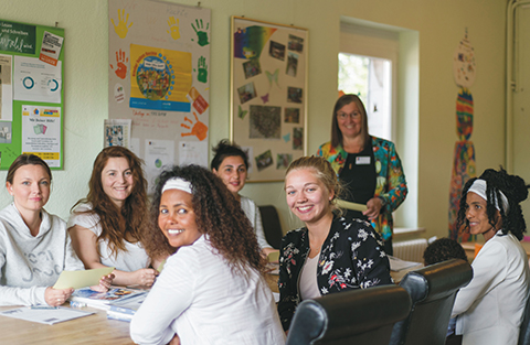 Frauen verschiedenen Alters sitzen am Tisch und l&auml;cheln in die Kamera